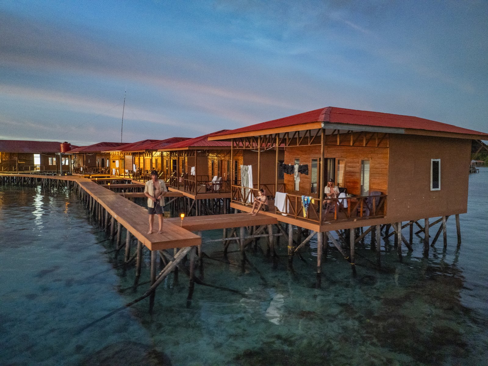 The overwater villas lit up above clear reef water at dusk