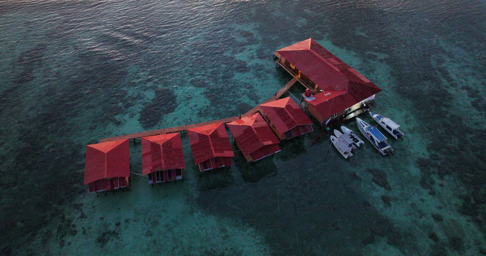 An overhead drone view of the villas standing above the reef, with boats alongside