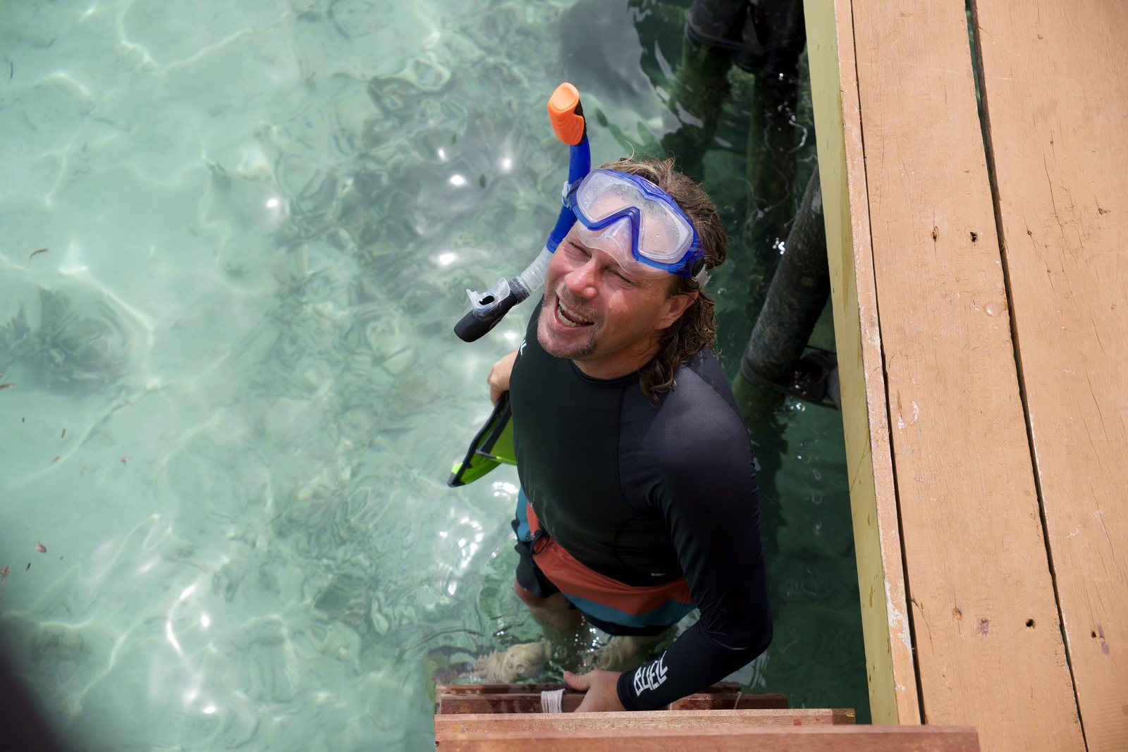 A guest wearing a snorkel mask climbing the villa steps from clear water