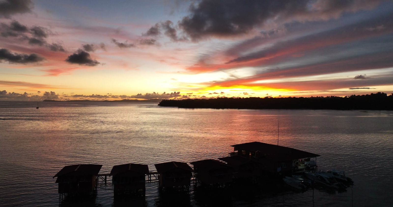 The overwater villas beneath a sunset sky, seen from a drone